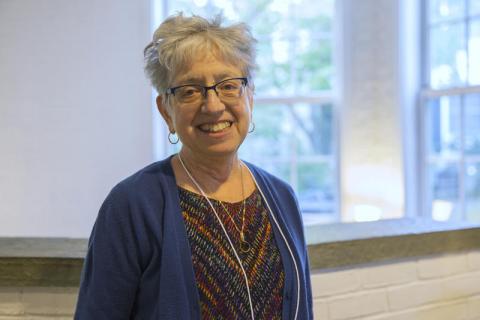 Headshot of Ann Tickamyer with short gray hair, glasses, multi-color blouse, and blue sweater.