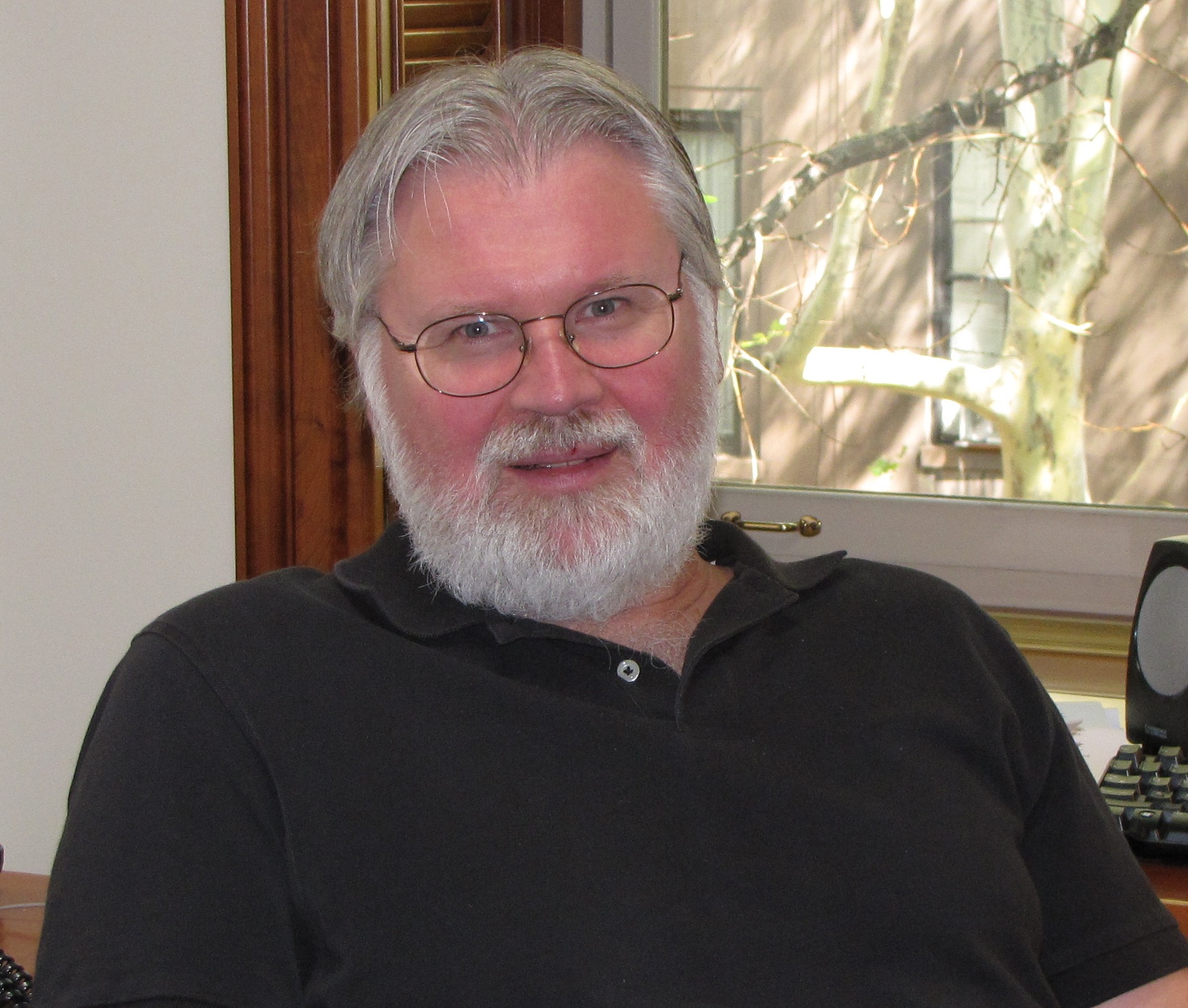 Douglas Massey head shot in black button-down shirt, white hair and beard