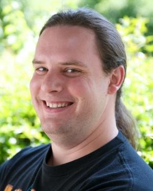Headshot of Timothy Brick with long brown hair and black t-shirt.