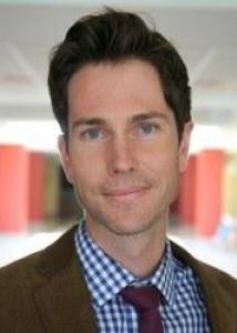Headshot of Andrew Fenelon with brown hair, a blue and white checkered shirt, red tie, and brown jacket.