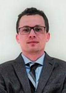 Headshot of Charles Seguin in front of a white wall wearing glasses and a suit and tie.