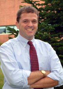 Headshot of Christopher Fowler crossing his arms wearing blue dress shirt and red tie.