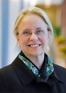 Headshot of Jill with light blonde hair, glasses, a black jacket, and green neck scarf.