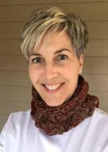 Headshot of Nancy Luke with short, blonde hair wearing a white top and brownish red scarf.
