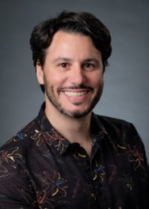 Headshot of Nicolas Sacco with black hair, beard, and black shirt with multi-colored print.