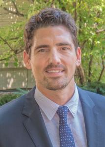 Headshot of Stephen Kodish outside with short, dark hair wearing suit and blue tie.