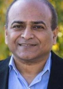 Headshot of Vasant Honavar outside wearing blue dress shirt and black suit jacket.