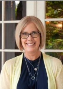 Headshot of Pamela with short blonde hair, glasses, blue shirt, and yellow sweater.